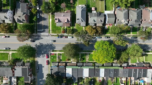 Residential street with cars, row houses, and lush trees. Top down aerial truck shot in American city.