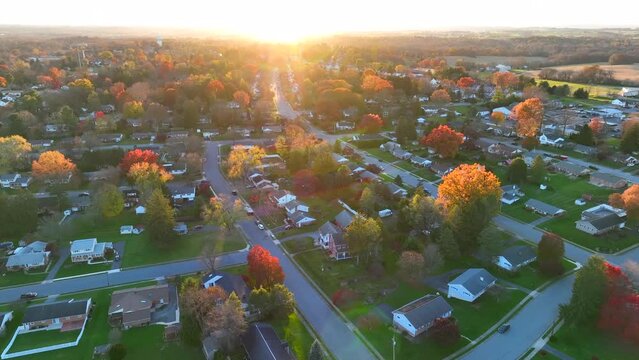 Small town in USA. Colorful autumn fall foliage in neighborhood. High aerial establishing shot of homes and houses in United States of America during sunset.