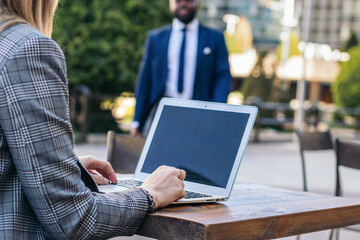 Close-up of unrecognizable businesswoman using laptop in outdoor cafe waiting for man in suit approaching for job interview