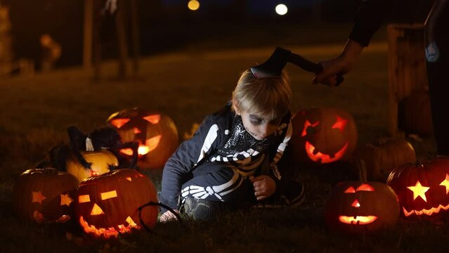 Two boys in the park with Halloween costumes, carved pumpkins with candles and decoration, playing