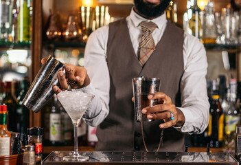 Close-up of the hands of a stylish black bartender preparing a cocktail in a shaker in a traditional cocktail bar