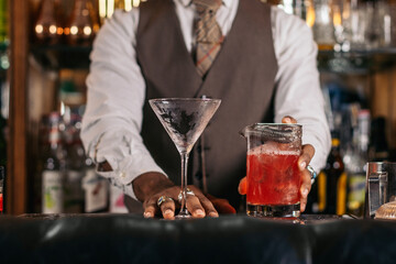 Close-up of the hands of a stylish black bartender preparing a cocktail in a traditional cocktail bar