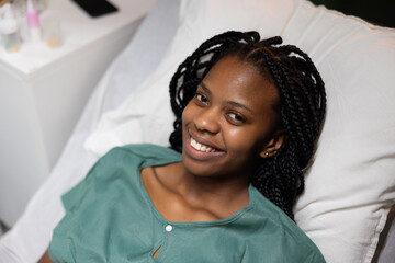 Happy delighted patient with braids lies on bed while recieves recovering after a bad accident.