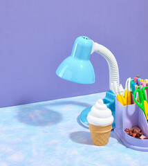 Fototapeta premium Work office table. A bright blue table lamp, a stationery stand with supplies for study and work. Fresh, cold, yummy ice cream in a waffle cup. Copy space for text.