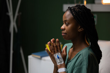 Young girl sitting on a bed in a ward, praying, worried about a complicated surgery.