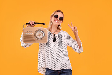Portrait of happy hippie woman with retro radio receiver showing peace sign on yellow background