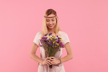 Portrait of smiling hippie woman with bouquet of flowers on pink background