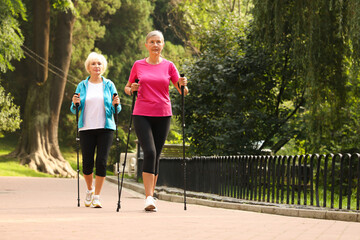 Two senior friends performing Nordic walking outdoors, space for text. Low angle view
