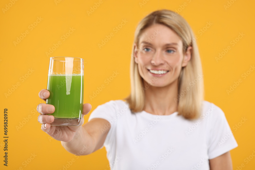 Poster Happy woman with glass of fresh celery juice on orange background, selective focus