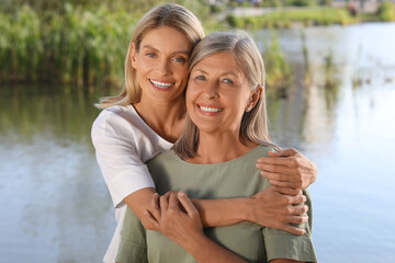 Family portrait of happy mother and daughter hugging near pond
