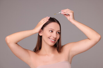 Beautiful woman applying serum onto hair on grey background