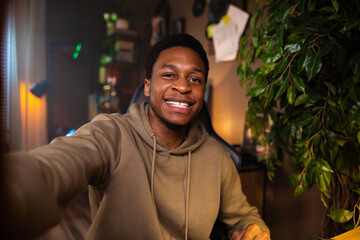 Delighted African man in living room points finger at camera signifying tha man guy technology...