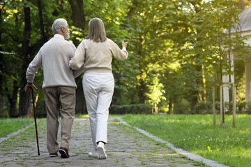 Fototapeta premium Senior man with walking cane and mature woman in park, back view. Space for text