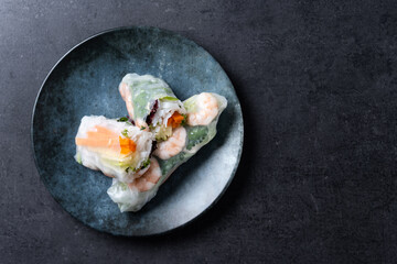 Vietnamese spring rolls with vegetables, rice noodles and prawns on black slate background. Top view. Copy space