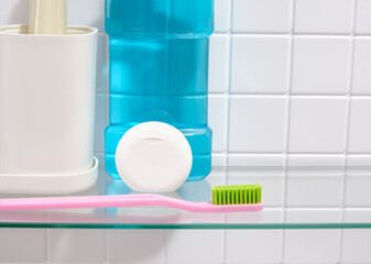 A pink toothbrush with green bristles, floss and blue mouthwash on a white tile background.