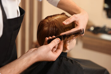 Professional hairdresser combing boy's hair in beauty salon, closeup