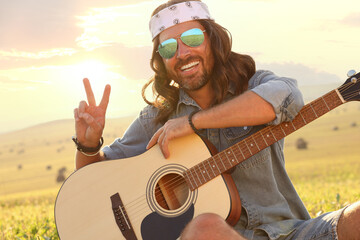 Happy hippie man with guitar showing peace sign in field