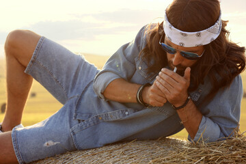 Hippie man smoking joint on hay bale in field