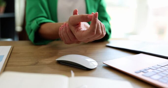 Business woman sitting at computer desk and suffering from pain in arm working in the office. Woman massaging wrist with carpal tunnel syndrome caused by prolonged keyboard and mouse use