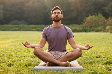 Man practicing yoga on mat outdoors. Lotus pose - Powered by Adobe