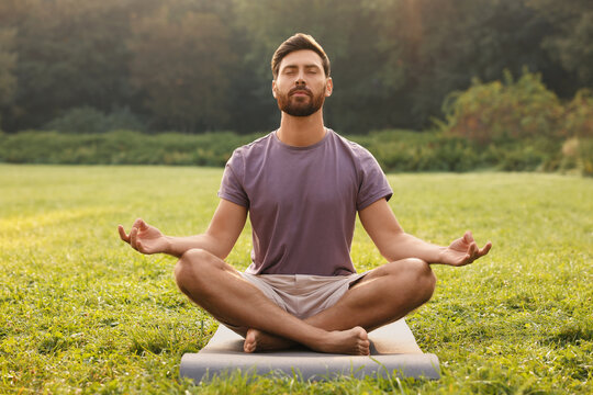 Man practicing yoga on mat outdoors. Lotus pose
