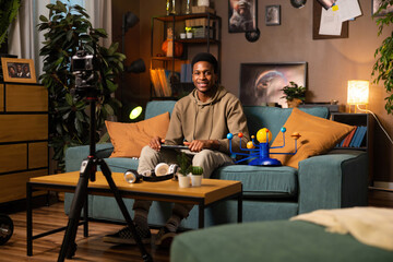 African American student blogger records video in her cozy living room, with laptop and camera in...