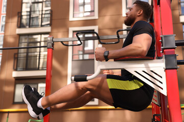 Man doing leg rise exercise at outdoor gym, low angle view