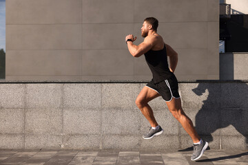 Fototapeta premium Young man running near building outdoors. Space for text