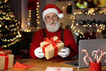 Fototapeta na wymiar Santa Claus holding gift box at his workplace in room decorated for Christmas
