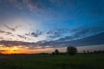 Fototapeta na wymiar Cloud in the sky after sunset over a green meadow, May evening