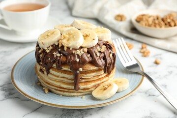 Tasty pancakes with chocolate spread, sliced banana and nuts served on white marble table, closeup