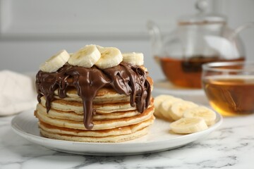 Tasty pancakes with chocolate spread and sliced banana served on white marble table, closeup