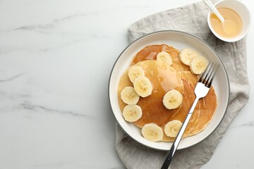 Tasty pancakes with sliced banana and honey served on white marble table, top view. Space for text