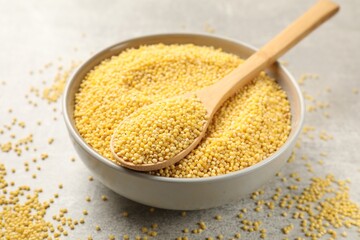 Millet groats in bowl and spoon on light grey table, closeup