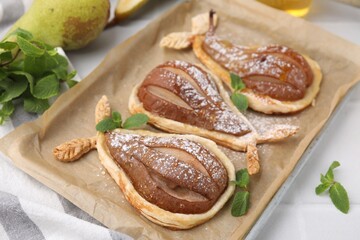 Delicious pears baked in puff pastry with powdered sugar and mint on white table, closeup