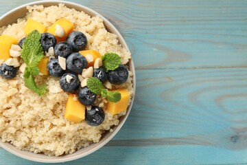 Tasty quinoa porridge with blueberries, pumpkin and mint in bowl on light blue wooden table, top view. Space for text