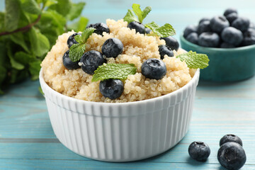 Tasty quinoa porridge with blueberries and mint in bowl on light blue wooden table, closeup
