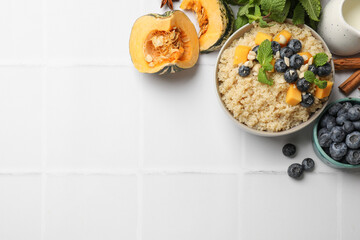 Flat lay composition with bowl of tasty quinoa porridge, blueberries and pumpkin on white tiled table. Space for text