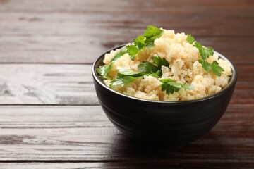 Tasty quinoa porridge with parsley in bowl on wooden table, closeup. Space for text