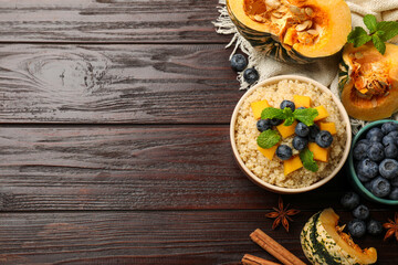 Flat lay composition with bowl of tasty quinoa porridge, pumpkin and blueberries on wooden table. Space for text