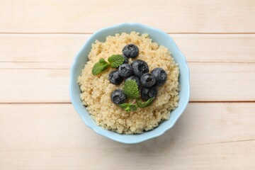 Tasty quinoa porridge with blueberries and mint in bowl on light wooden table, top view