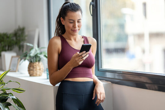 Shot of sporty woman using mobile phone after training at home..
