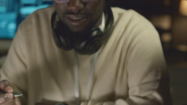 Tilt up shot of Black male software engineer taking notes in copybook and talking with Biracial colleague while co-working in dark office at night