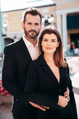 Beautiful fashion woman and her handsome elegant boyfriend in black suit. Sexy brunette model in jacket. Fashionable confident couple posing in street. Brutal man and female outdoors