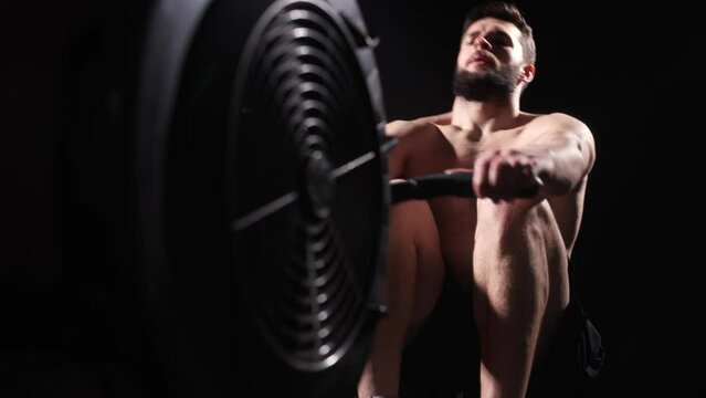 Young strong bearded bodybuilder doing a low row of rope pulleys while sitting. fitness male athlete training rowing machine exercise intense endurance training.