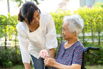 Caregive talk and help Asian elderly woman holding flower, smile and happy in the sunny garden.