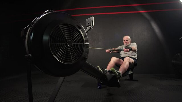 Close Up of 50s or 60s Old Man Training Hands at Rowing Machine. Workout of Healthy Elderly Male or Fast Warming Up Inside Fitness Hall. Active Lifestyle or Wellness of Senior Confident Person at Gym