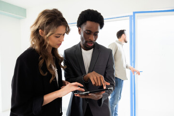 Blonde young beautiful woman talking with african americal real estate agent choosing house discussing house home future homeowners while handsome busy husband observing house potential clients.