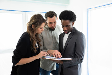 Concentrated young family discussing new building plan with rela estate manager looking examining...