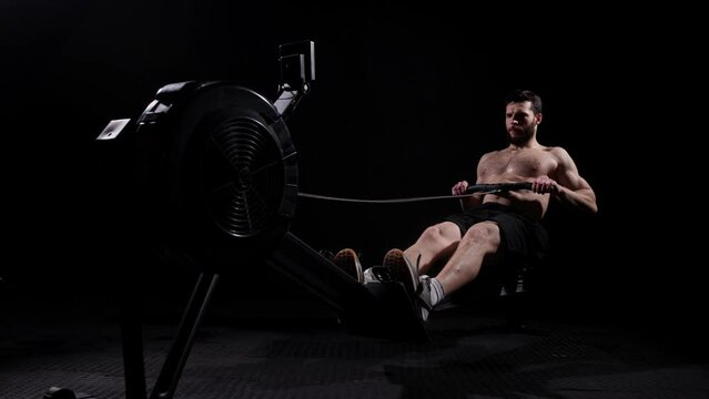 Young strong bearded bodybuilder doing a low row of rope pulleys while sitting. fitness male athlete training rowing machine exercise intense endurance training.
